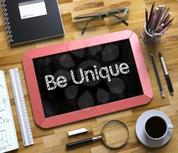 Be Unique Handwritten on Small Chalkboard. Be Unique Handwritten on Red Small Chalkboard. Top View of Wooden Office Desk with a Lot of Business and Office Supplies on It. 3d Rendering.