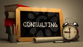 Handwritten Consulting on a Chalkboard. Composition with Chalkboard and Stack of Books, Alarm Clock and Rolls of Paper on Blurred Background. Toned Image.