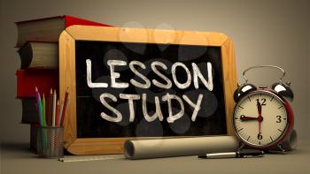 Handwritten Lesson Study on a Chalkboard. Composition with Chalkboard and Stack of Books, Alarm Clock and Rolls of Paper on Blurred Background. Toned Image.