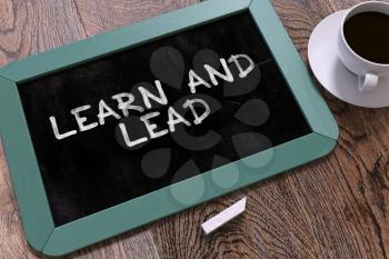 Handwritten Learn and Lead on a Blue Chalkboard. Top View Composition with Chalkboard and White Cup of Coffee.  Inspirational Quote.