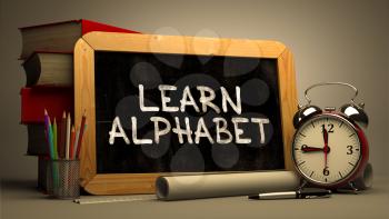 Learn Alphabet.  Inspirational Quote Handwritten on Chalkboard. Time Concept. Composition with Chalkboard and Stack of Books, Alarm Clock and Scrolls on Blurred Background. Toned Image.