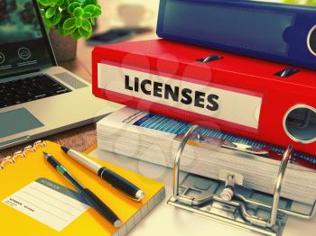 Red Office Folder with Inscription Licenses on Office Desktop with Office Supplies and Modern Laptop. Business Concept on Blurred Background. Toned Image.