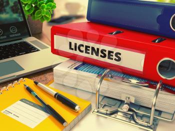 Red Office Folder with Inscription Licenses on Office Desktop with Office Supplies and Modern Laptop. Business Concept on Blurred Background. Toned Image.