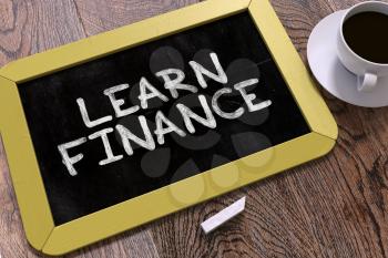 Learn Finance - Yellow Chalkboard with Hand Drawn Inspirational Quote and White Cup of Coffee on Wooden Table. Top View.