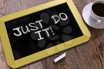 Just Do It. Motivational Quote Hand Drawn on Yellow Chalkboard on Wooden Table. Business Background. Top View.