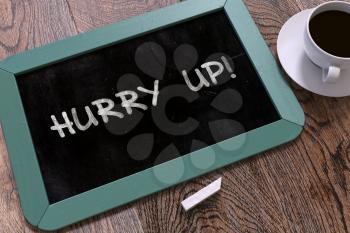 Hurry Up - Blue Chalkboard with Hand Drawn Motivation Quote and White Cup of Coffee on Wooden Table. Top View.