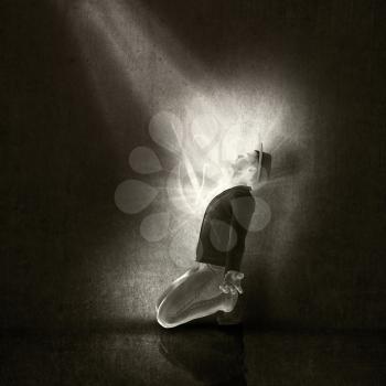 Image of a man on his knees worshipping to a ray of light in a grunge interior