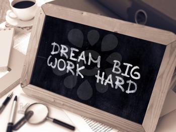 Dream Big Work Hard - Chalkboard with Hand Drawn Text, Stack of Office Folders, Stationery, Reports on Blurred Background. Toned Image. 3d Render.