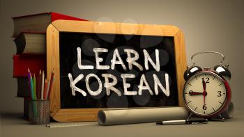 Learn Korean Handwritten on Chalkboard. Time Concept. Composition with Chalkboard and Stack of Books, Alarm Clock and Scrolls on Blurred Background. Toned Image. 3D Render.
