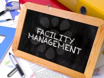 Facility Management - Chalkboard with Hand Drawn Text, Stack of Office Folders, Stationery, Reports on Blurred Background. Toned Image. 3D Render.