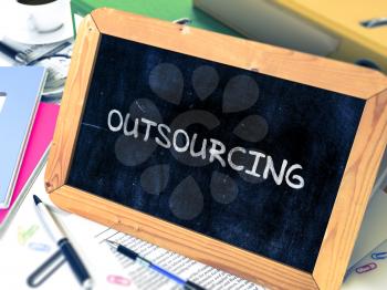 Outsourcing Handwritten by Chalk on a Blackboard. Composition with Small Chalkboard on Background of Working Table with Office Folders, Stationery, Reports. Blurred Background. Toned Image. 3D Render.