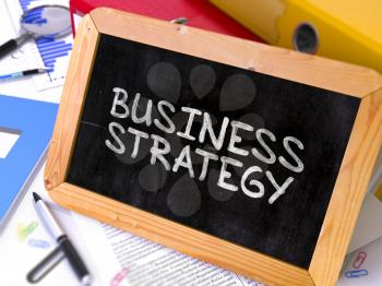 Business Strategy Handwritten on a Chalkboard. Composition with Small Chalkboard on Background of Working Table with Office Folders, Stationery, Reports. Blurred Background. Toned Image. 3D Render.
