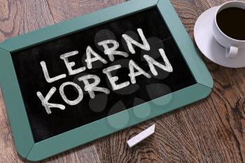 Learn Korean - Blue Chalkboard with Hand Drawn Text and White Cup of Coffee on Wooden Table. Top View. 3D Render.