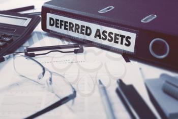 Deferred Assets - Office Folder on Background of Working Table with Stationery, Glasses, Reports. Business Concept on Blurred Background. Toned Image.