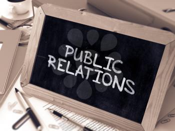 Public Relations Handwritten by White Chalk on a Blackboard. Composition with Small Chalkboard on Background of Working Table with Office Folders, Stationery, Reports. Blurred, Toned Image. 3D Render.