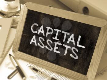 Capital Assets - Chalkboard with Hand Drawn Text, Stack of Office Folders, Stationery, Reports on Blurred Background. Toned Image. 3D Render.
