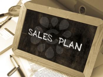 Sales Plan Handwritten on Chalkboard. Composition with Small Chalkboard on Background of Working Table with Ring Binders, Office Supplies, Reports. Blurred Background. Toned Image. 3D Render.