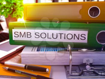 Green Office Folder with Inscription SMB - Small Business Solution - Solutions on Office Desktop with Office Supplies and Modern Laptop. SMB Solutions Business Concept on Blurred Background. 3D.