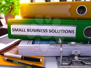Green Ring Binder with Inscription Small Business Solutions on Background of Working Table with Office Supplies and Laptop. Small Business Solutions Business Concept on Blurred Background. 3D Render.
