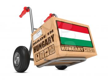 Cardboard Box with Flag of Hungary and Made in Hungary Slogan on Hand Truck White Background. Free Shipping Concept.
