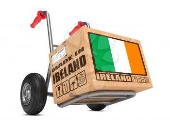 Cardboard Box with Flag of Ireland and Made in Ireland Slogan on Hand Truck White Background. Free Shipping Concept.