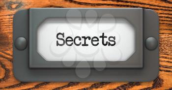 Secrets Inscription on File Drawer Label on a Wooden Background.