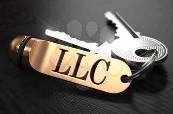 Keys and Golden Keyring with the Word LLC - Limited Legal Liability - over Black Wooden Table with Blur Effect.