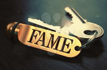 Keys and Golden Keyring with the word Fame over Black Wooden Table with Blur Effect. Toned Image.