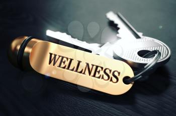 Keys and Golden Keyring with the Word Wellness over Black Wooden Table with Blur Effect. Toned Image.