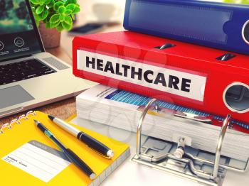 Healthcare - Red Office Folder on Background of Working Table with Stationery, Laptop and Reports. Business Concept on Blurred Background. Toned Image.