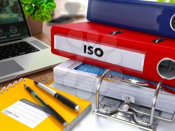 Red Ring Binder with Inscription ISO on Background of Working Table with Office Supplies, Laptop, Reports. Toned Illustration. Business Concept on Blurred Background.