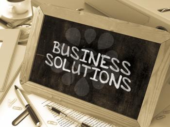 Business Solutions Handwritten by white Chalk on a Blackboard. Composition with Small Chalkboard on Background of Working Table with Office Folders, Stationery, Reports. Blurred Background. Toned Imag
