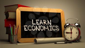 Learn Economics. Motivational Quote Handwritten by white Chalk on a Blackboard. Composition with Small Chalkboard and Stack of Books, Alarm Clock and Rolls of Paper on Blurred Background. Toned Image.