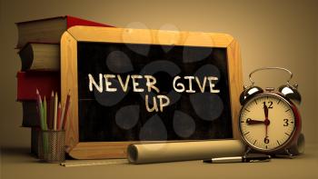 Never Give Up Handwritten by white Chalk on a Blackboard. Composition with Small Chalkboard and Stack of Books, Alarm Clock and Rolls of Paper on Blurred Background. Toned Image.