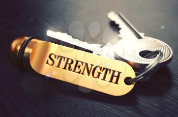 Keys and Golden Keyring with the Word Strength over Black Wooden Table with Blur Effect. Toned Image.