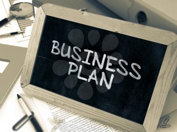 Handwritten Business Plan on a Chalkboard. Composition with Chalkboard and Ring Binders, Office Supplies, Reports on Blurred Background. Toned Image.