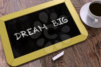 Dream Big - Yellow Chalkboard with Hand Drawn Text and White Cup of Coffee on Wooden Table.  Inspirational Quote. Top View.
