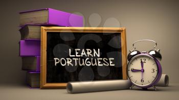 Learn Portuguese - Chalkboard with Hand Drawn Inspirational Quote, Stack of Books, Alarm Clock and Rolls of Paper on Blurred Background. Toned Image.