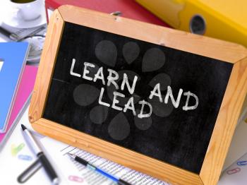 Learn and Lead - Chalkboard with Hand Drawn Motivation Quote, Stack of Office Folders, Stationery, Reports on Blurred Background. Toned Image.