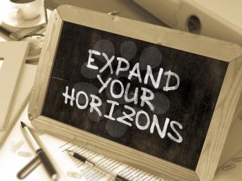 Expand Your Horizons. Motivation Quote on a Blackboard. Composition with Small Chalkboard on Background of Working Table with Office Folders, Stationery, Reports. Blurred, Toned Image.