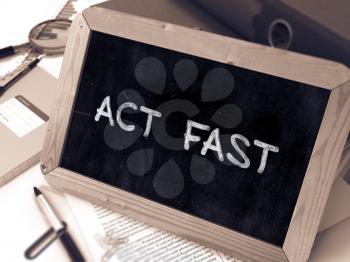 Act Fast Handwritten by white Chalk on a Blackboard. Composition with Small Chalkboard on Background of Working Table with Office Folders, Stationery, Reports. Blurred, Toned Image.
