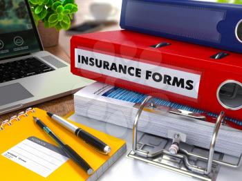Red Ring Binder with Inscription Insurance Forms on Background of Working Table with Office Supplies, Laptop, Reports. Toned Illustration. Business Concept on Blurred Background.
