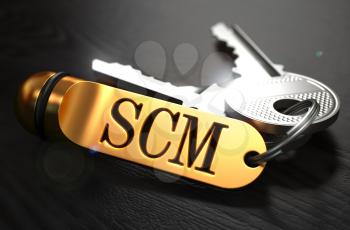 Keys and Golden Keyring with the Word SCM - Supply Chain Management - over Black Wooden Table with Blur Effect.