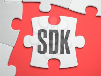 SDK -  Software Development Kit - Text on Puzzle on the Place of Missing Pieces. Scarlett Background. Close-up. 3d Illustration.