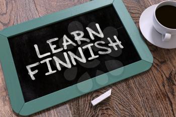 Learn Finnish Handwritten by white Chalk on a Blackboard. Composition with Small Blue Chalkboard and Cup of Coffee. Top View.