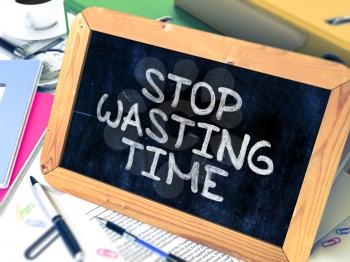 Stop Wasting Time - Chalkboard with Hand Drawn Text, Stack of Office Folders, Stationery, Reports on Blurred Background. Toned Image.